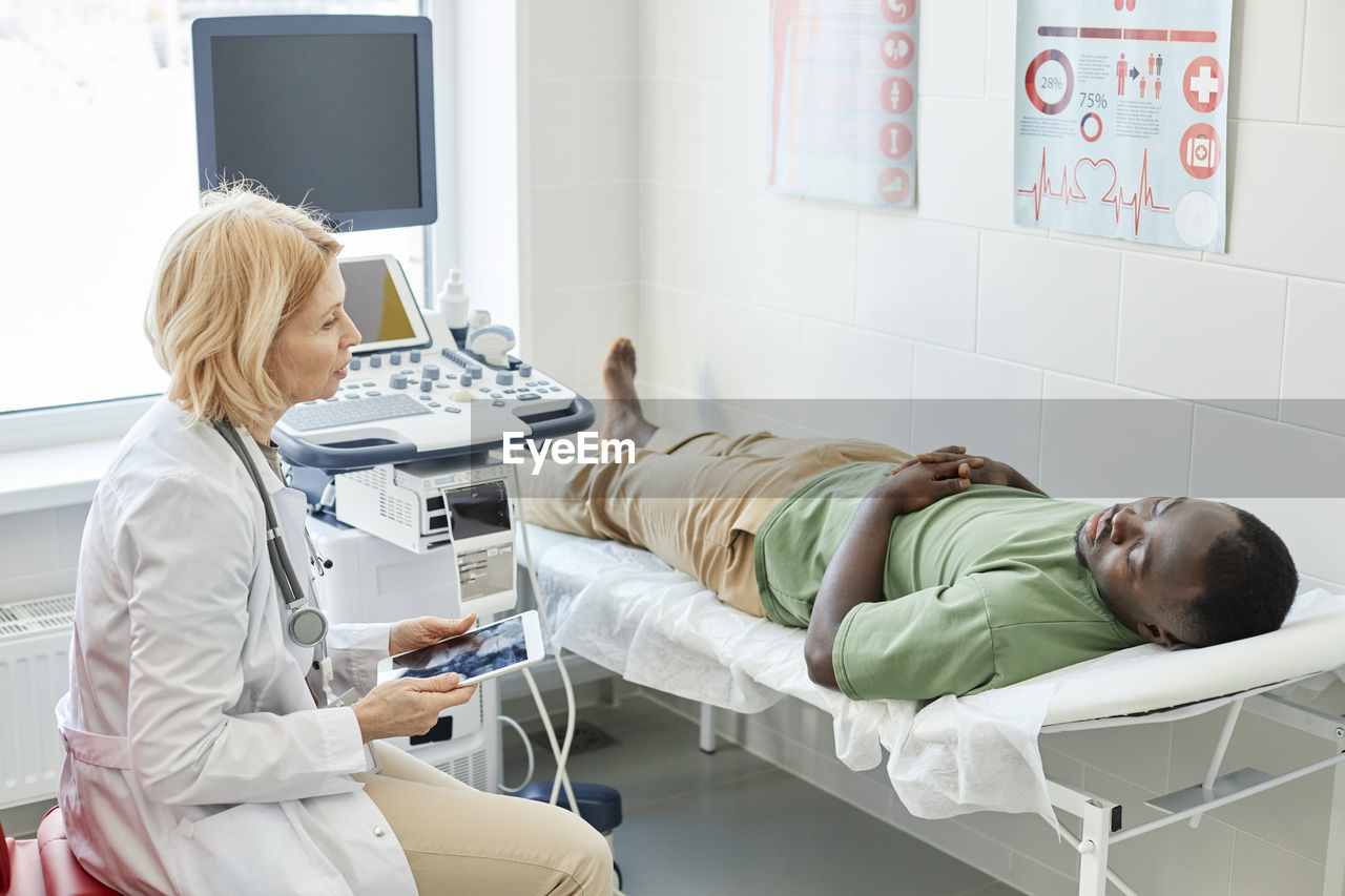 Doctor talking with patient lying on bed doing ultrasound in clinic