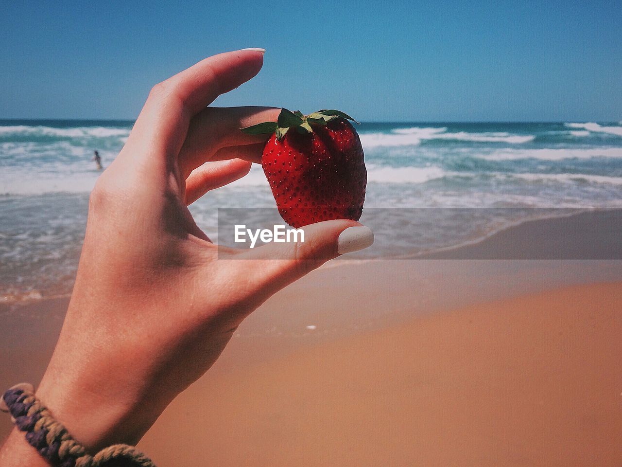 Woman holding strawberry at beach against sky