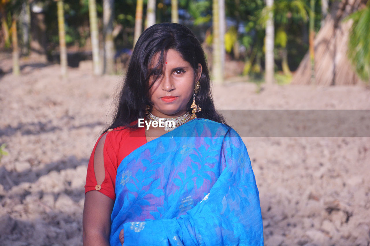 Portrait of girl wearing sari standing against trees