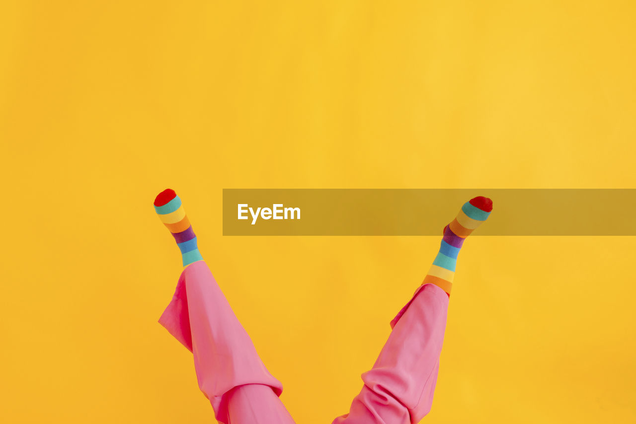 Feet of woman wearing multi colored socks against yellow background