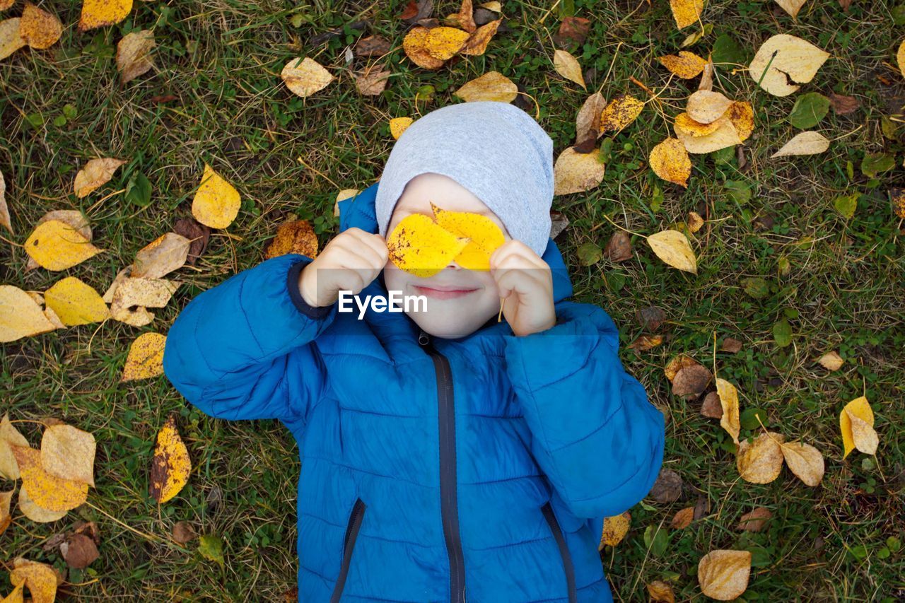 High angle view of boy holding autumn leaves while lying on field