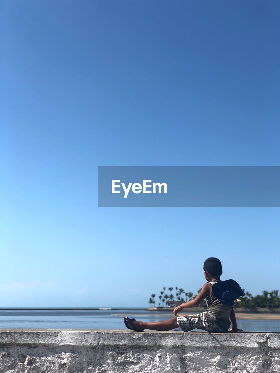 MAN SITTING AT BEACH AGAINST CLEAR SKY