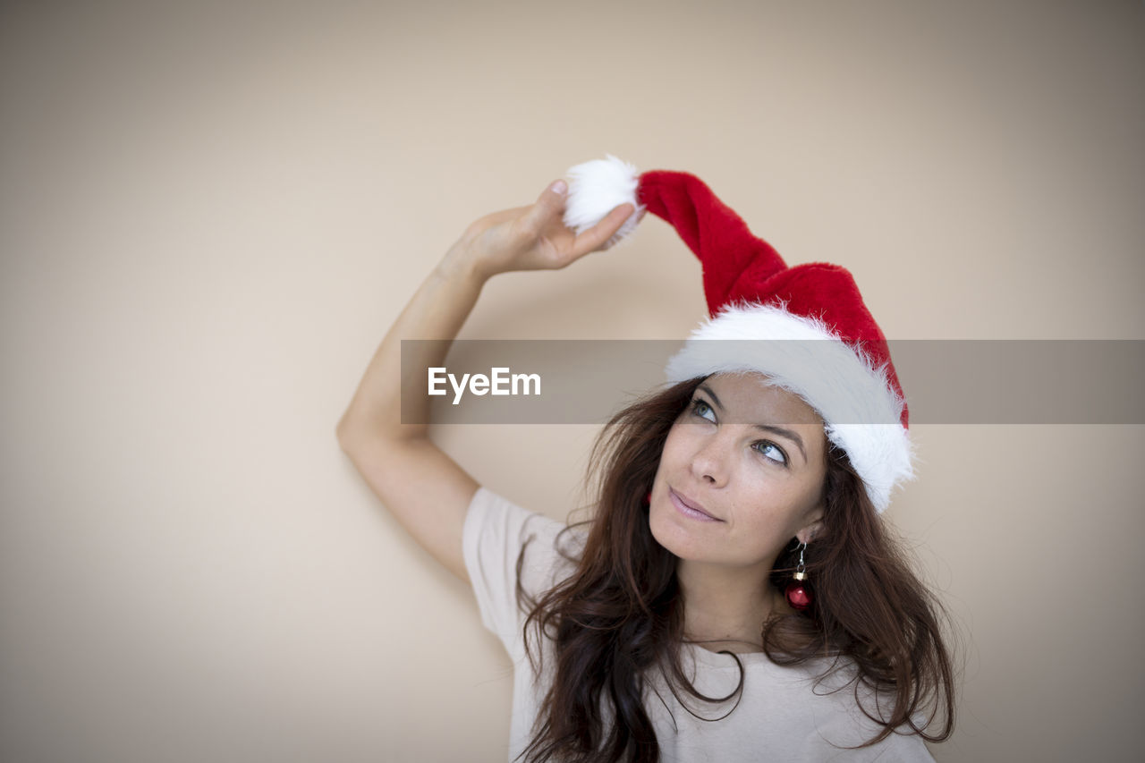 portrait of smiling young woman wearing santa hat against wall