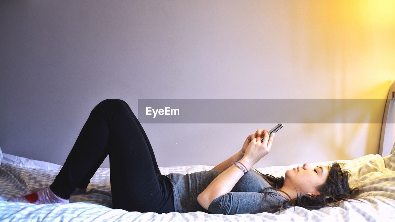 Side view of woman using mobile phone while lying on bed at home