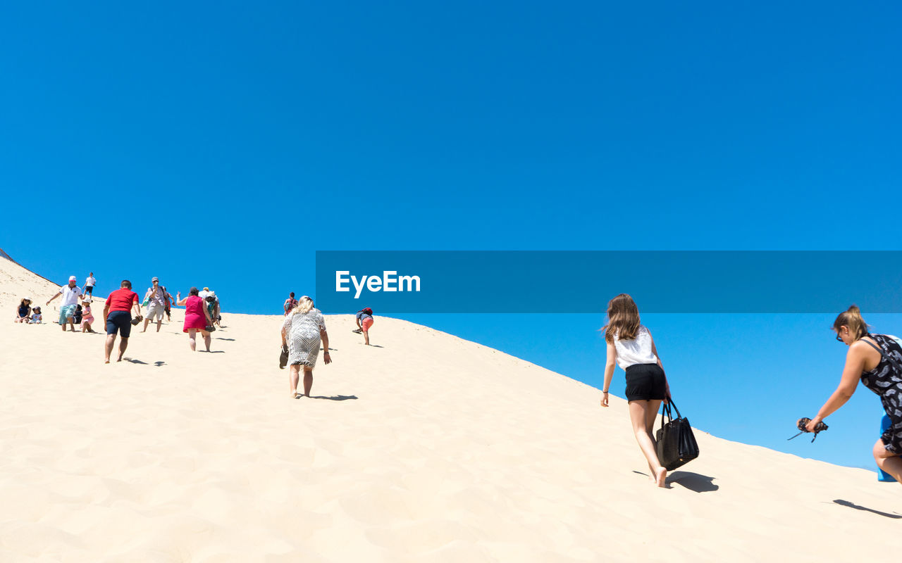 People walking on sand at beach against clear blue sky