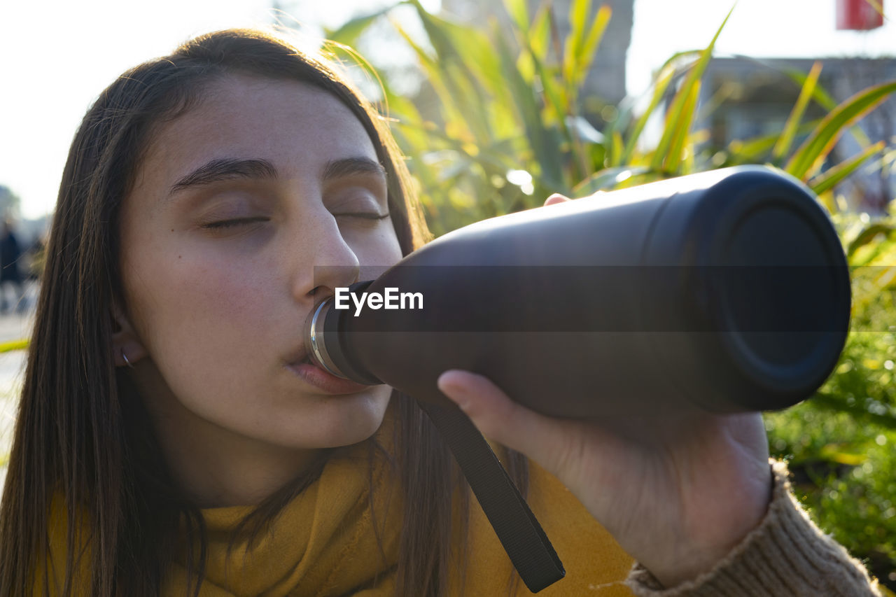 Young woman drinking from a black thermos.