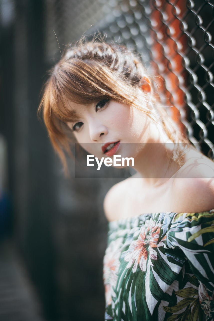 Portrait of young woman standing against fence