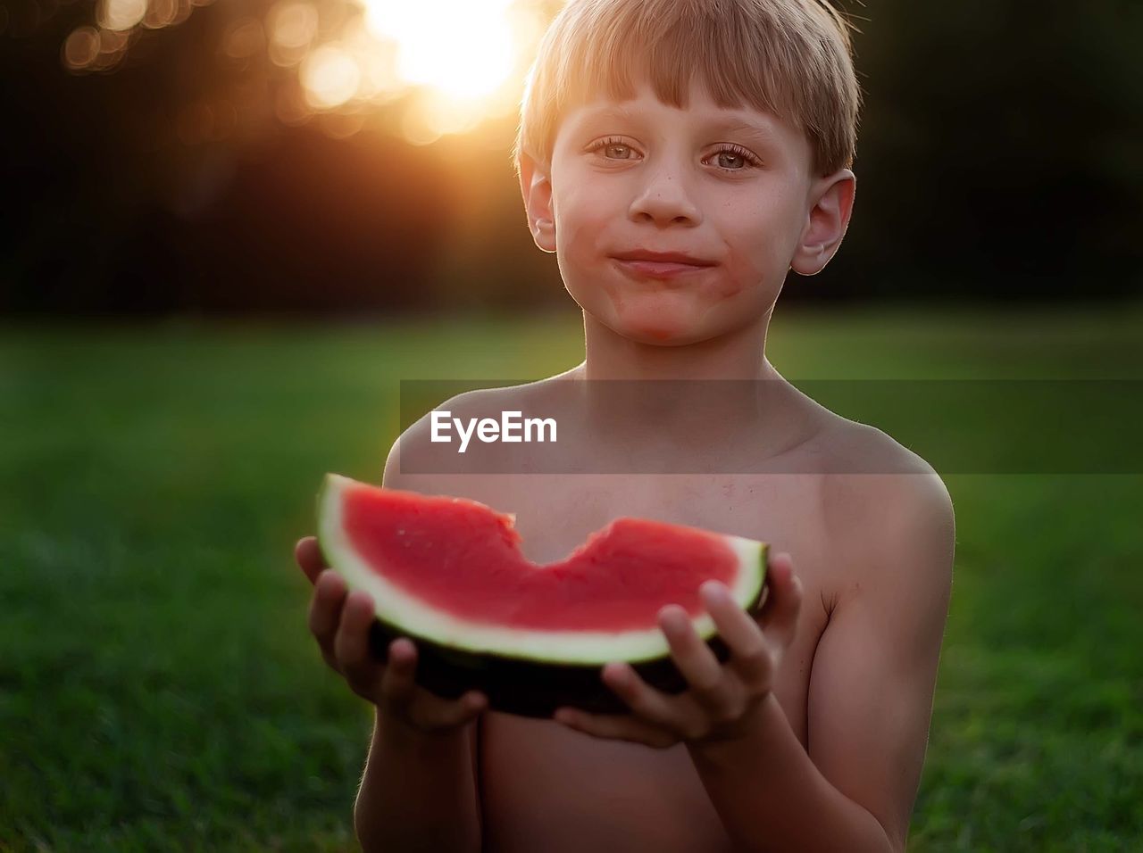 Portrait of shirtless boy eating watermelon during sunset