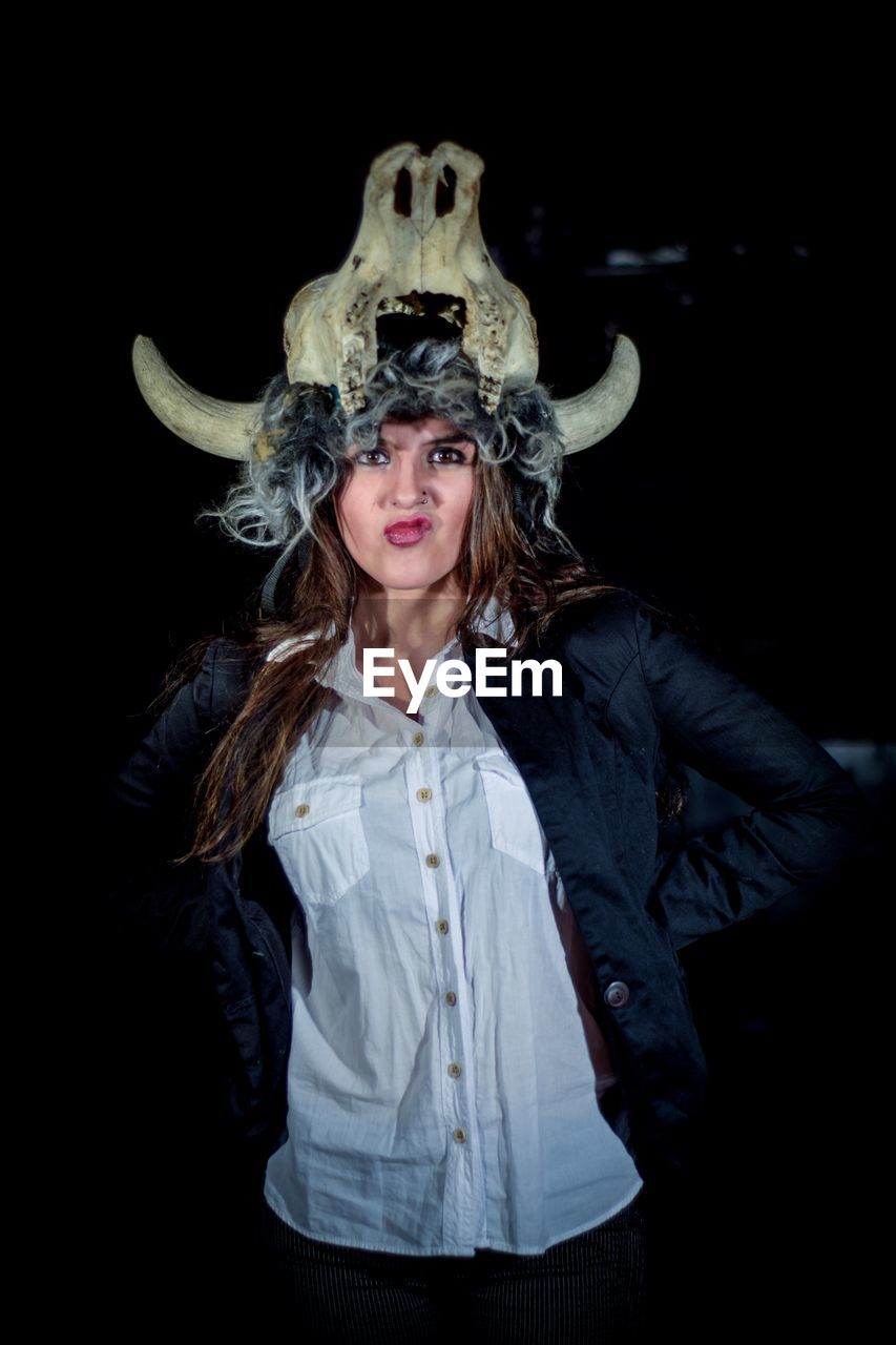 Portrait of angry young woman wearing animal skull on head over black background