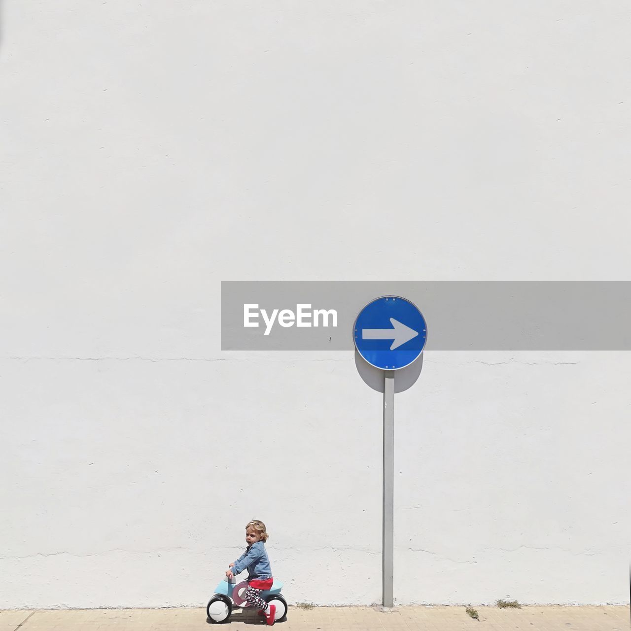 Girl riding tricycle against arrow symbol by wall