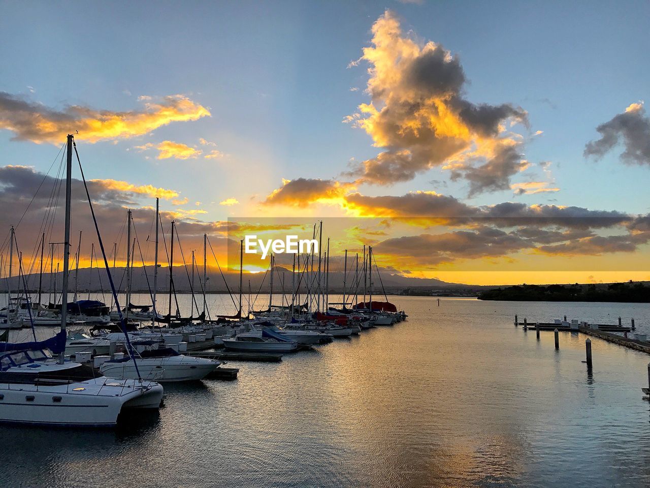 Sailboats moored on sea against sky during sunset