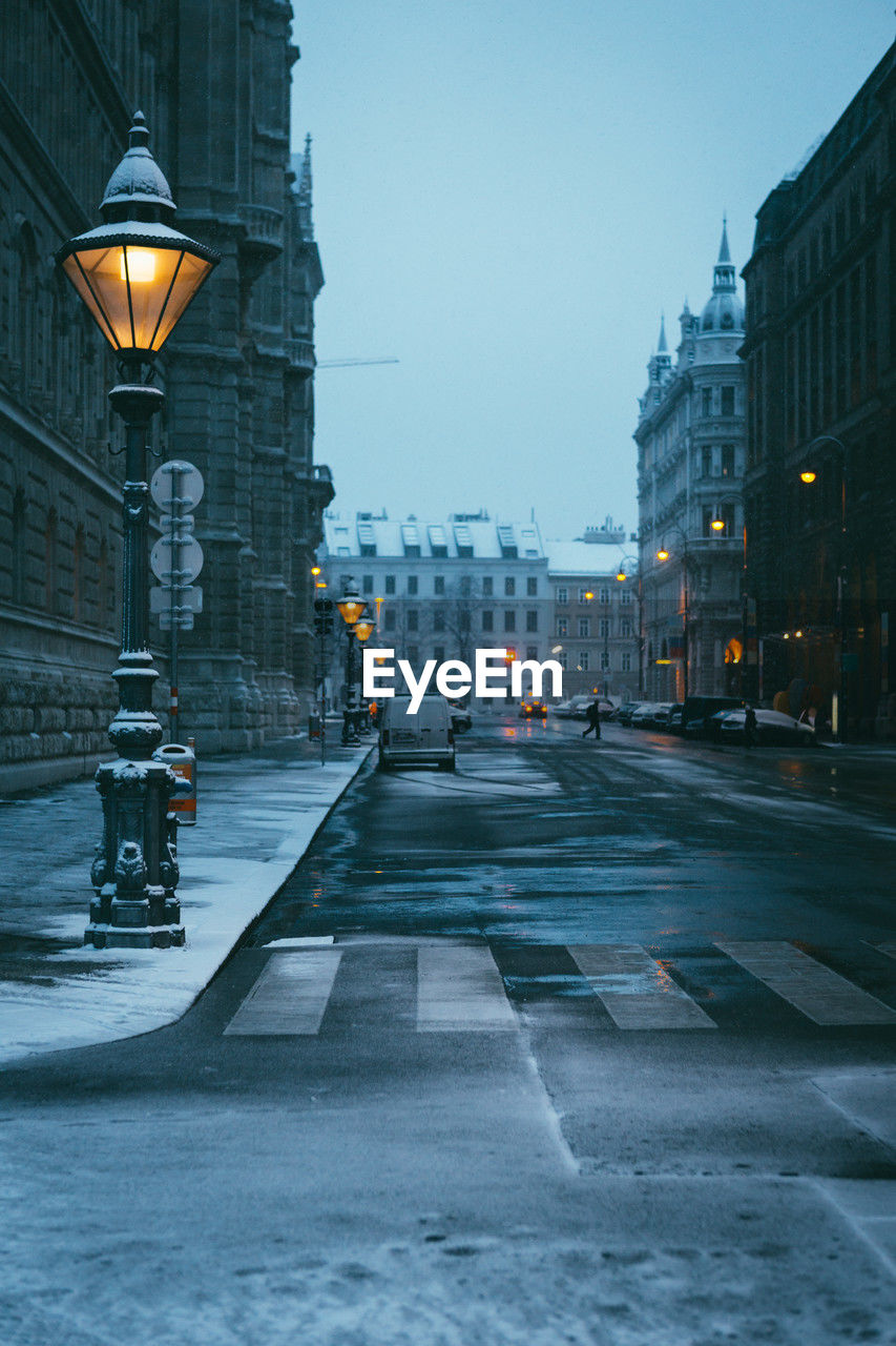 A snow-covered old lantern in the early morning and a street stretching into the distance