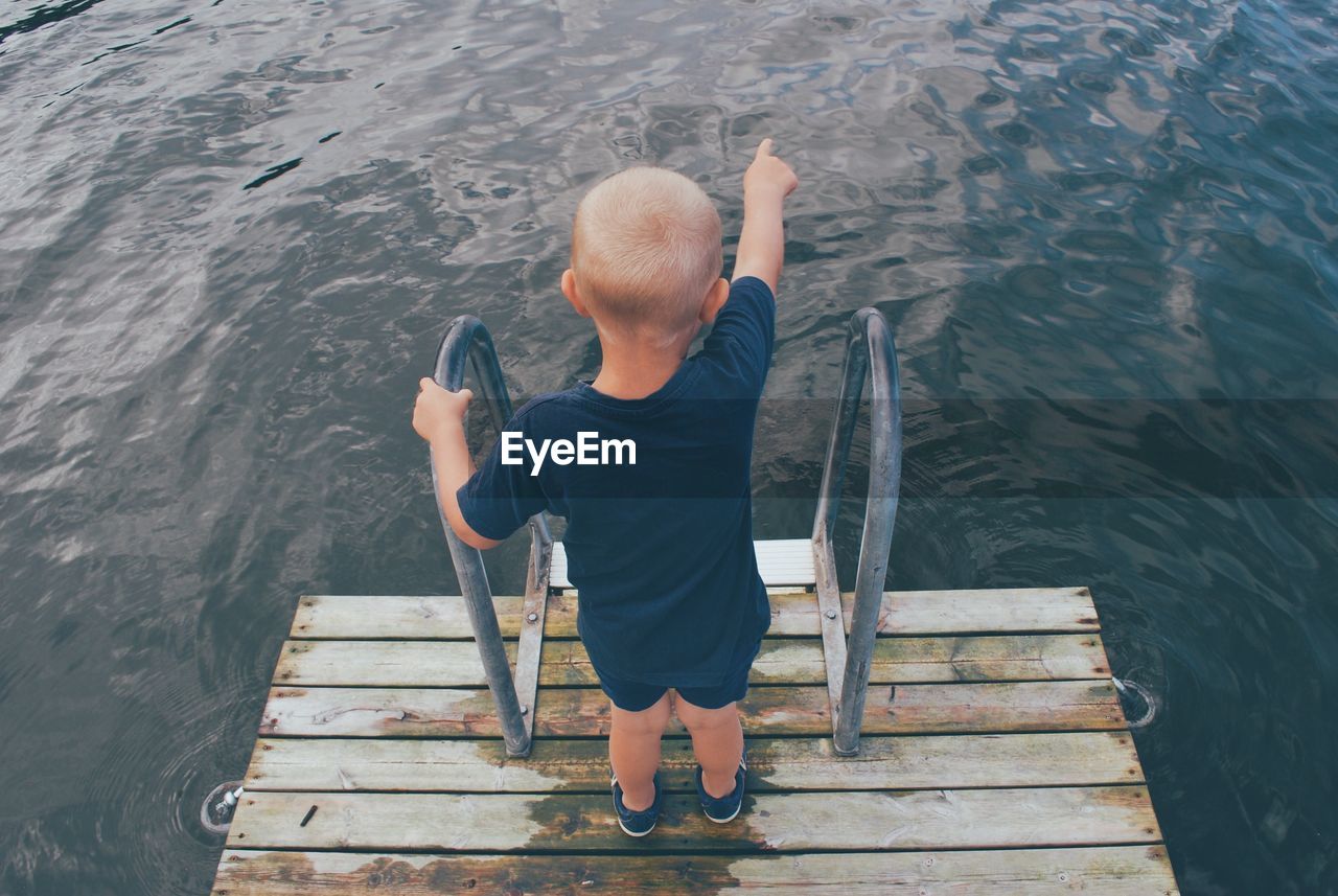 Rear view of boy standing on pier over lake