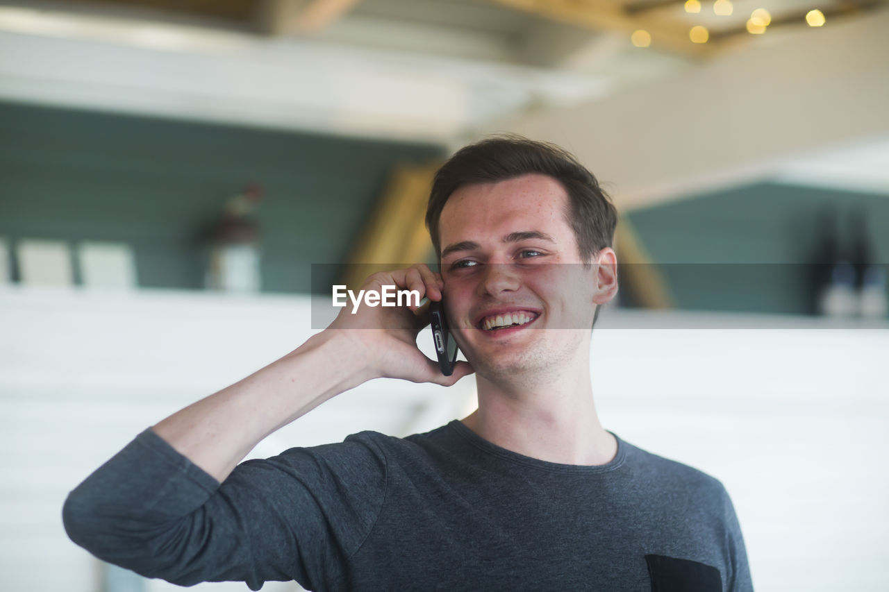 Young man wit smartphone standing in room