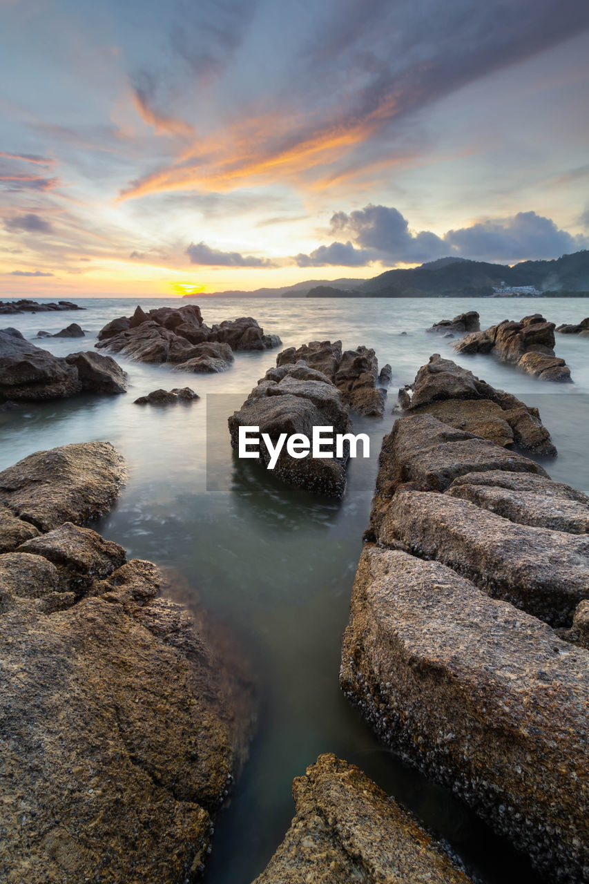 Rocks on beach against sky during sunset