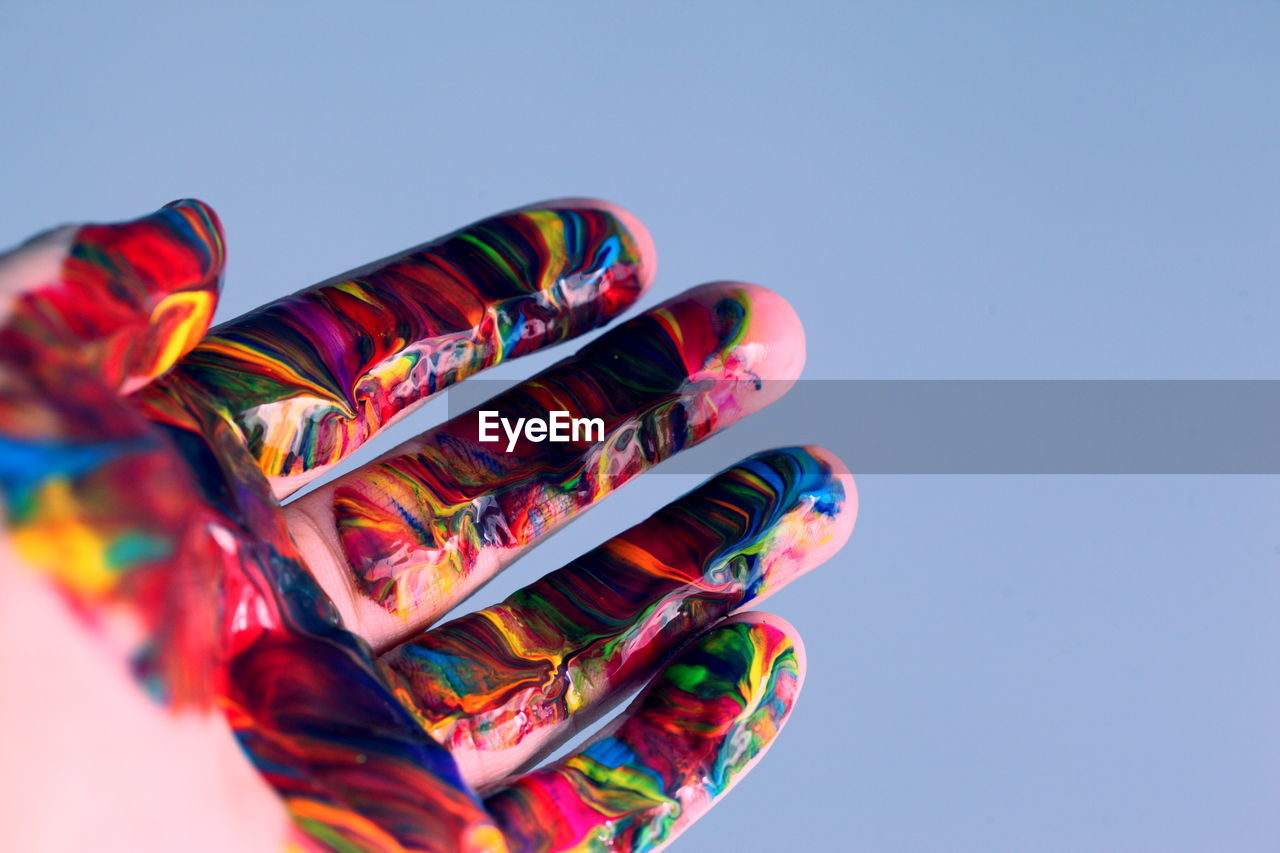 Close-up of cropped hand with watercolor paints against clear sky