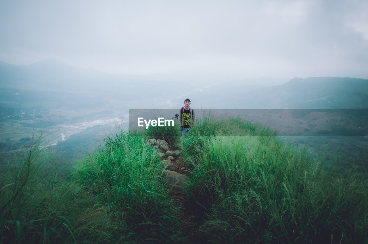 Hiker standing on mountain against sky during foggy weather