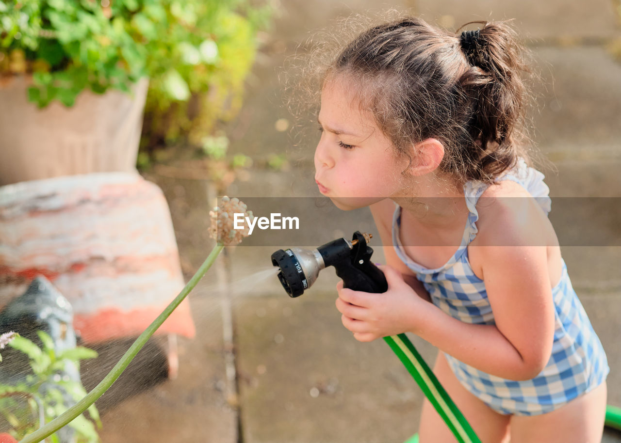 Young girl is watering plants in the backyard while wearing a bathing suit