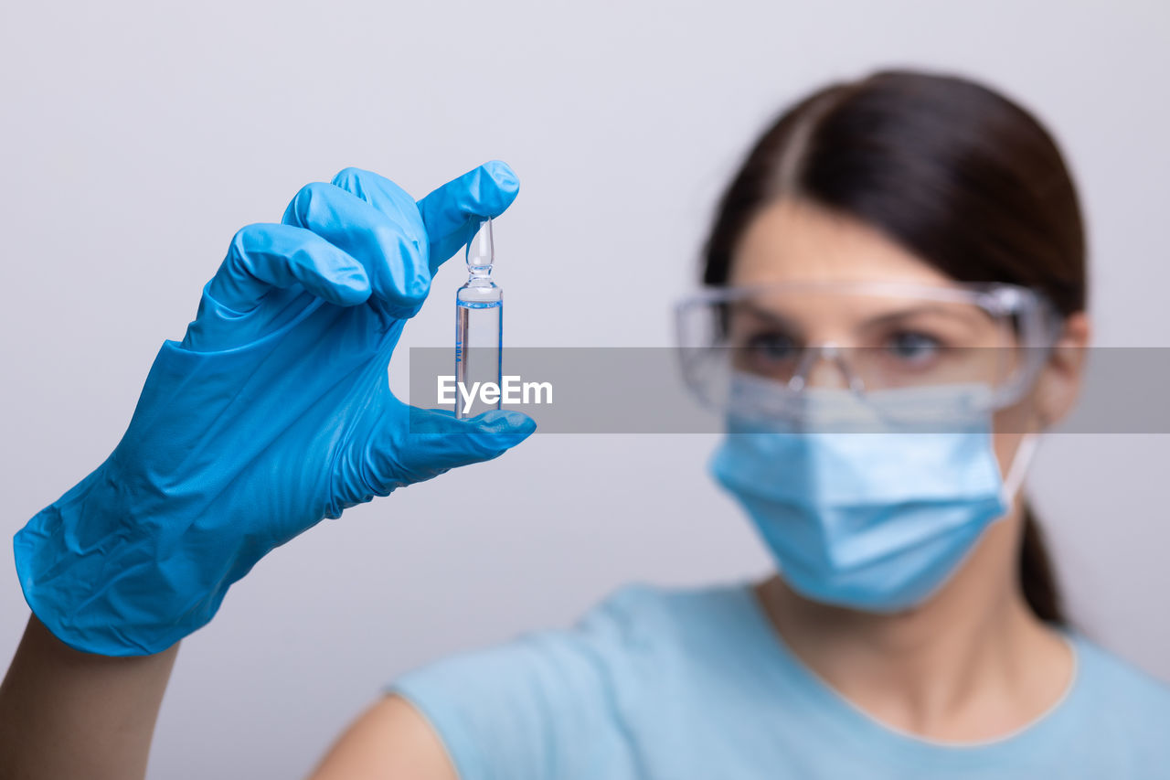 Doctor wearing mas holding vial against gray background