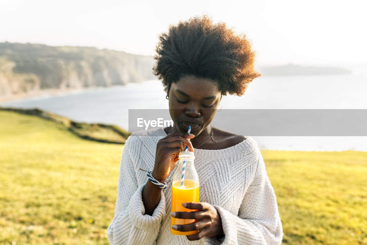 Young woman drinking orange juice at the coast