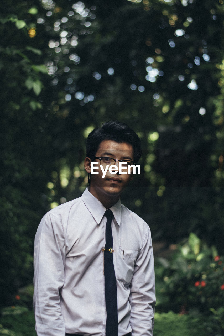 Portrait of young man standing against trees in park