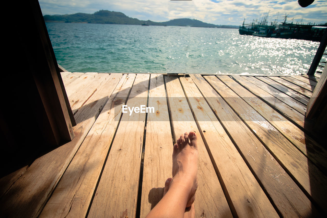 Low section of woman sitting on wooden floor of a bungalow with the view of the sea