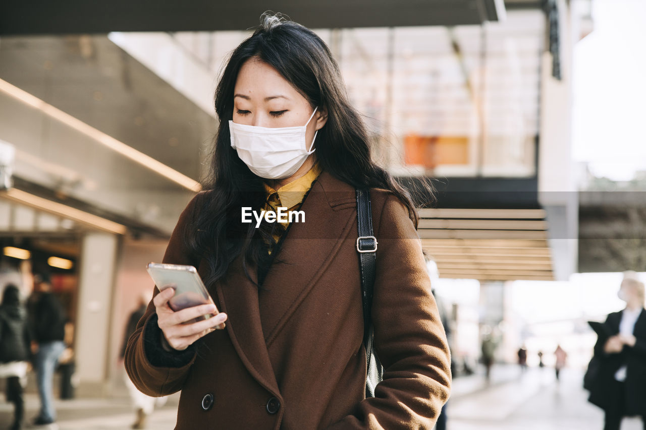 Woman walking in street with face mask using smartphone