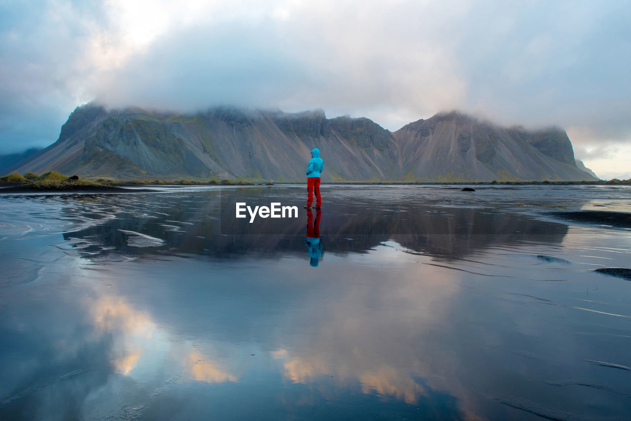 Reflection of a trekking woman and of the vestrahorn mountain in the atlantic ocean, hofn, iceland