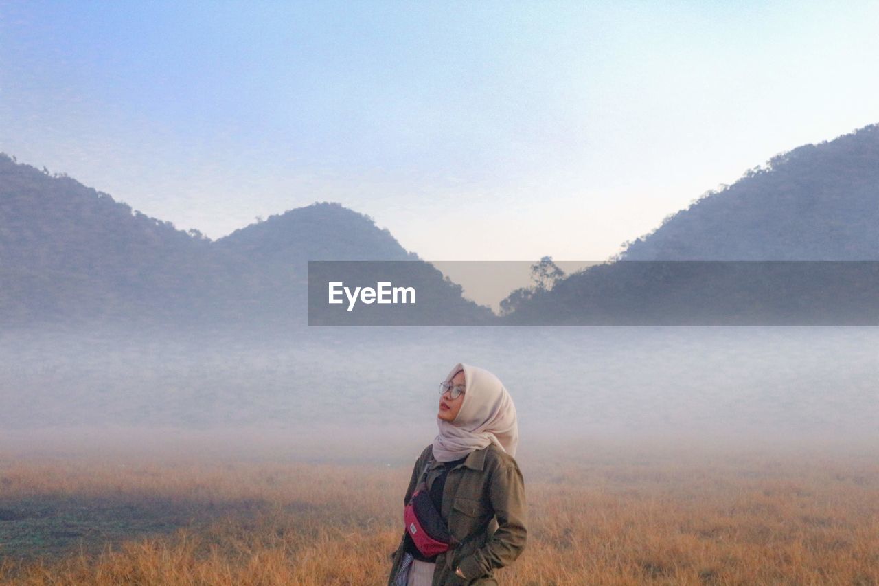 Young woman in hijab looking away while sanding against mountain range