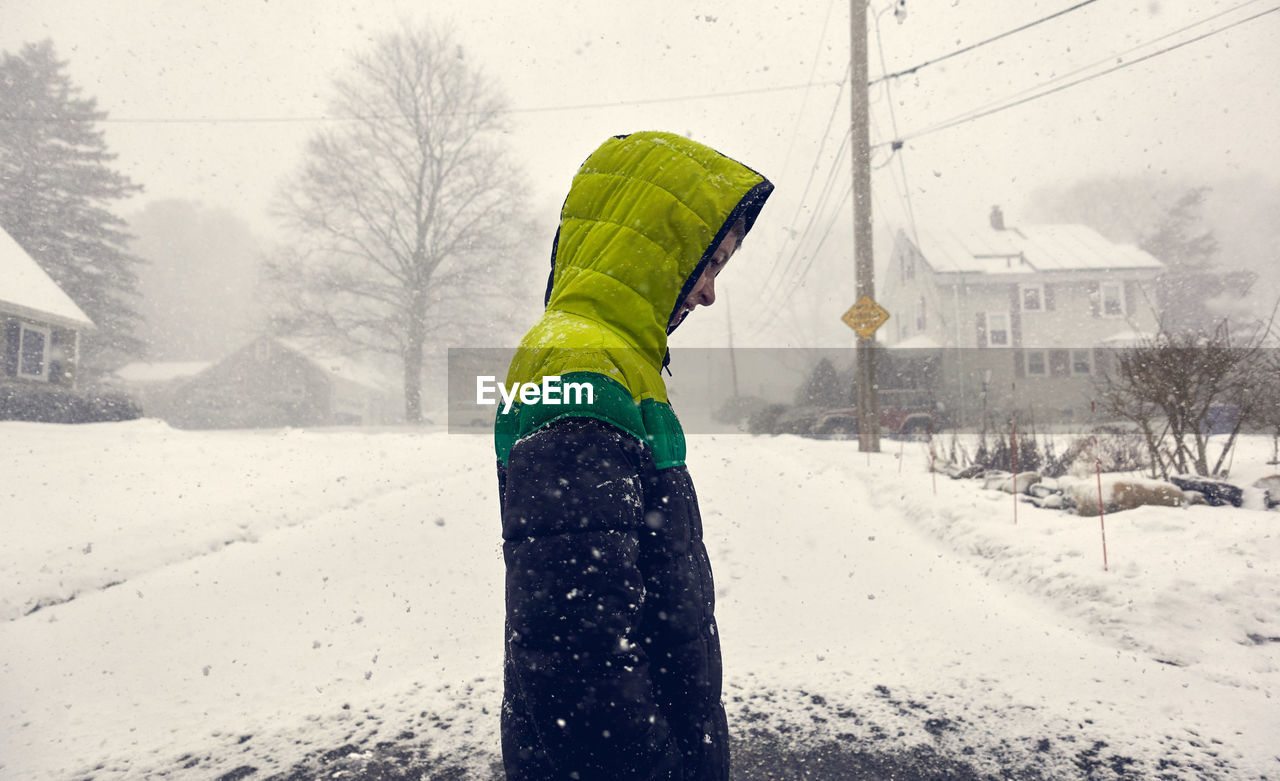 Side view of boy standing on road by snow covered land during winter