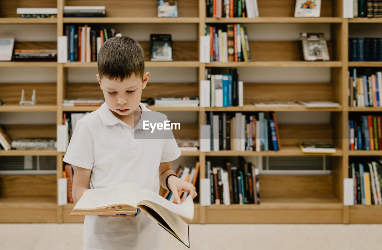 A boy stands in the library and reads a book while standing. preparing for homework. 