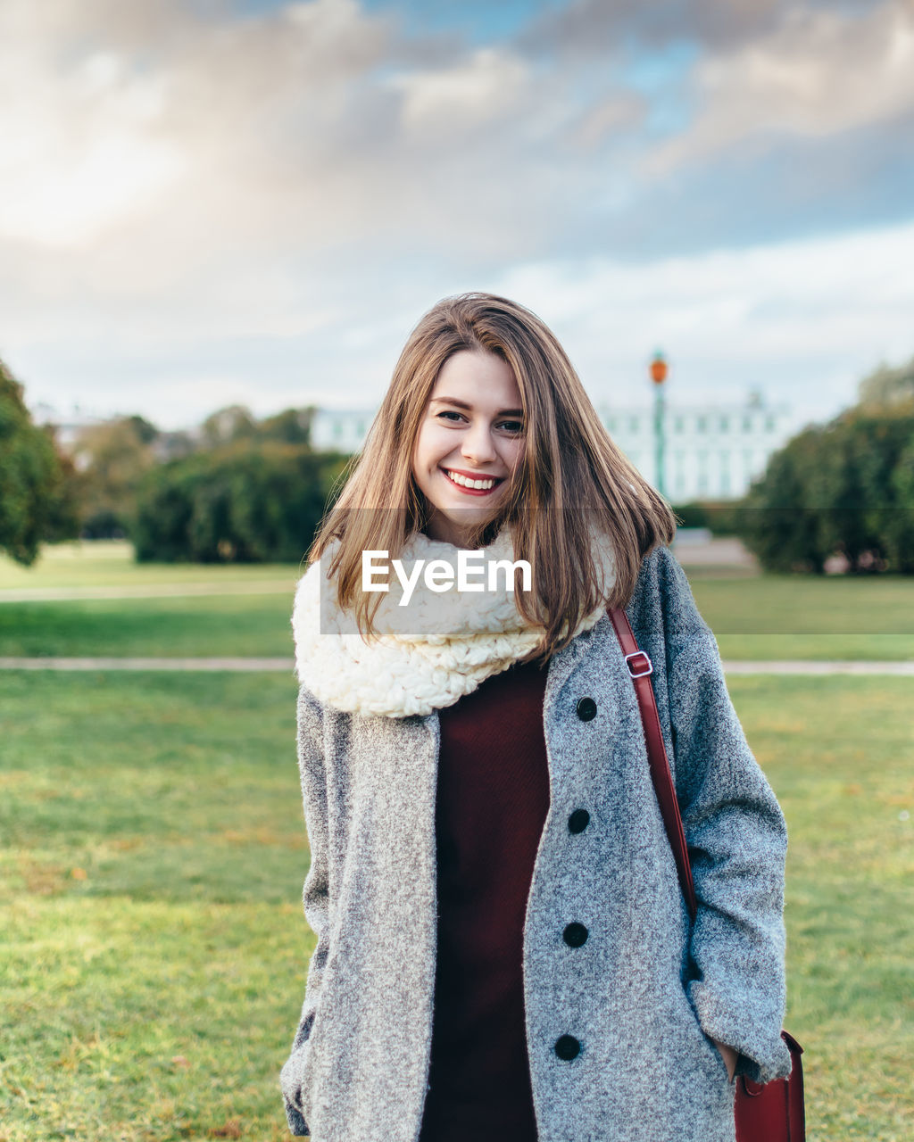 Portrait of smiling young woman in park against sky