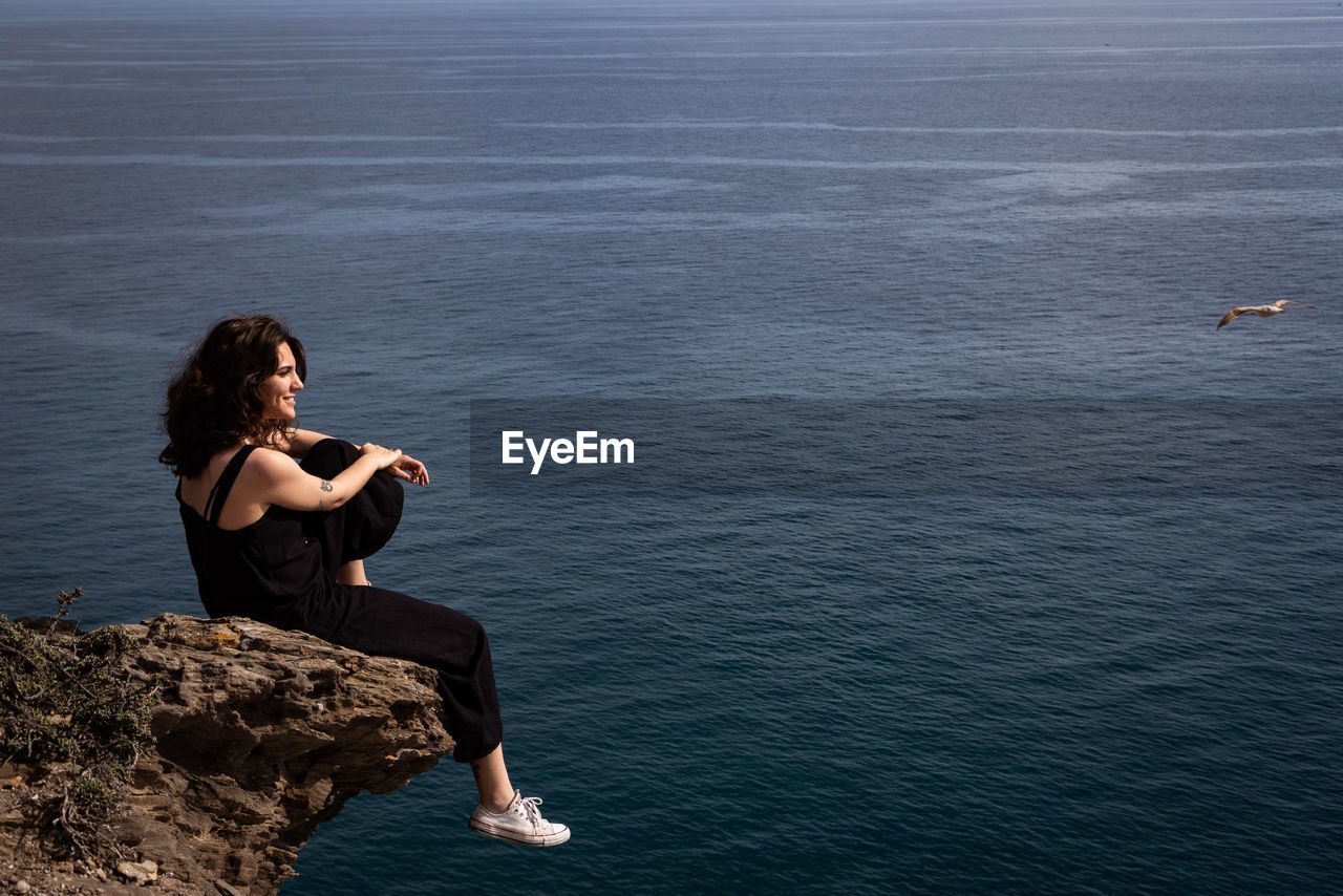 Side view of young woman sitting on rock by sea