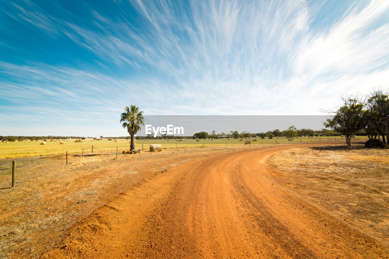 Dirt road amidst field against sky