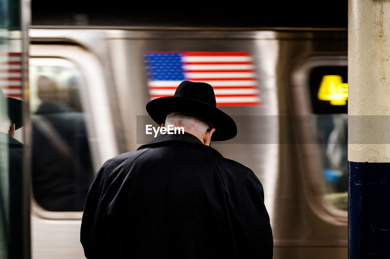 Rear view of man wearing hat against train at subway station