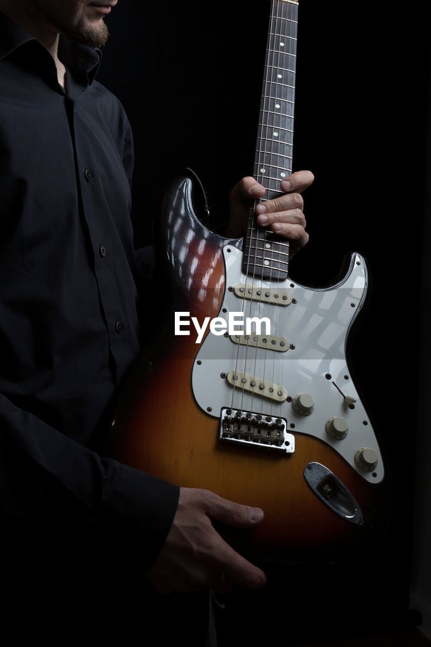 midsection of man playing guitar against black background