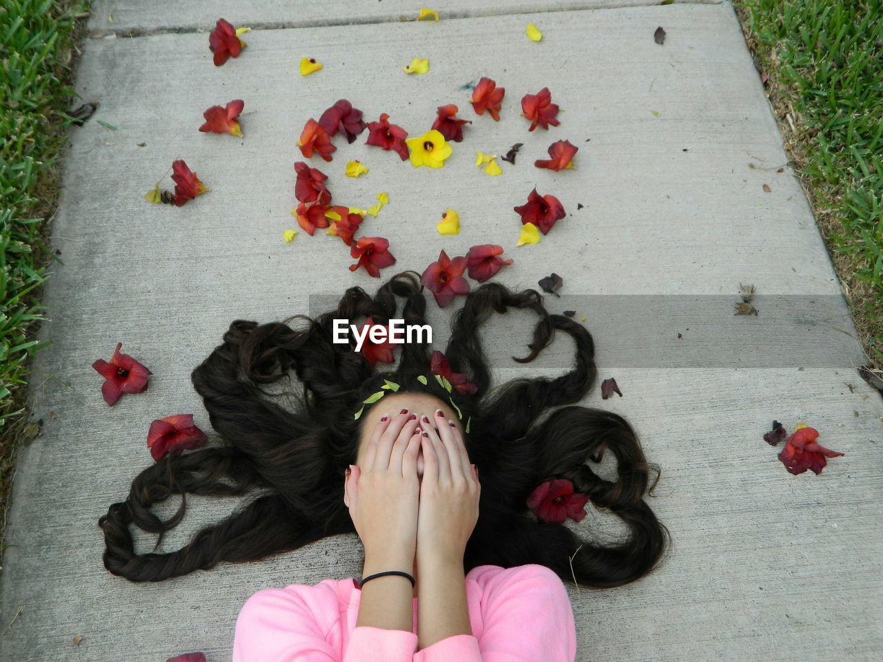 High angle view of woman hiding face behind hands with heart shape flower petals on footpath