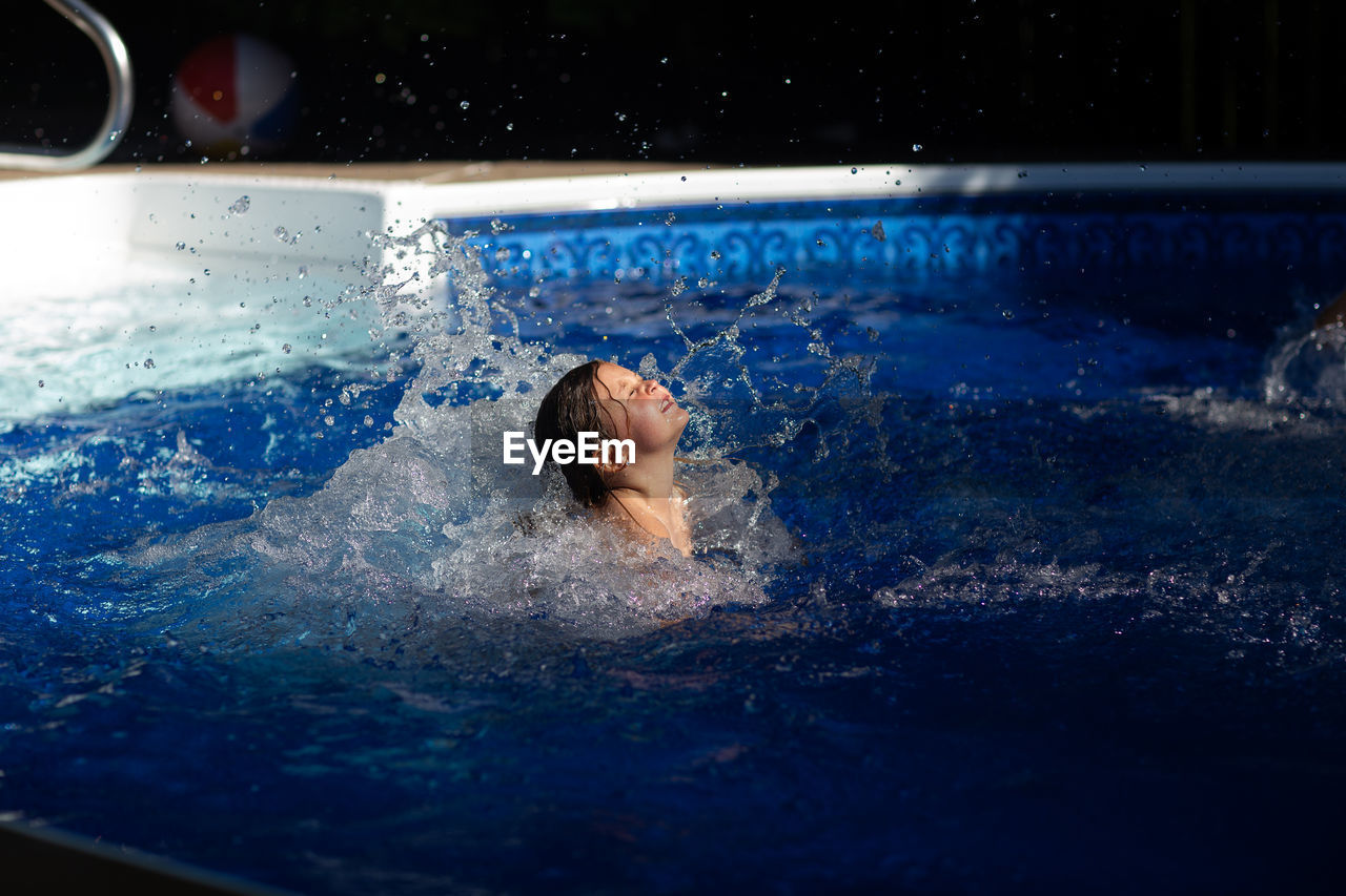 Girl splashing water while swimming in pool