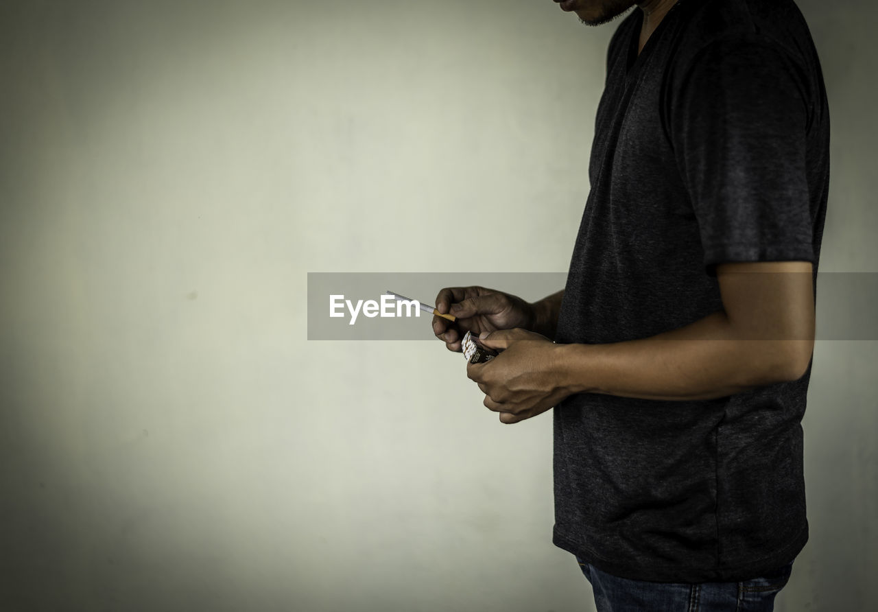 MAN HOLDING SMART PHONE WHILE STANDING ON WALL