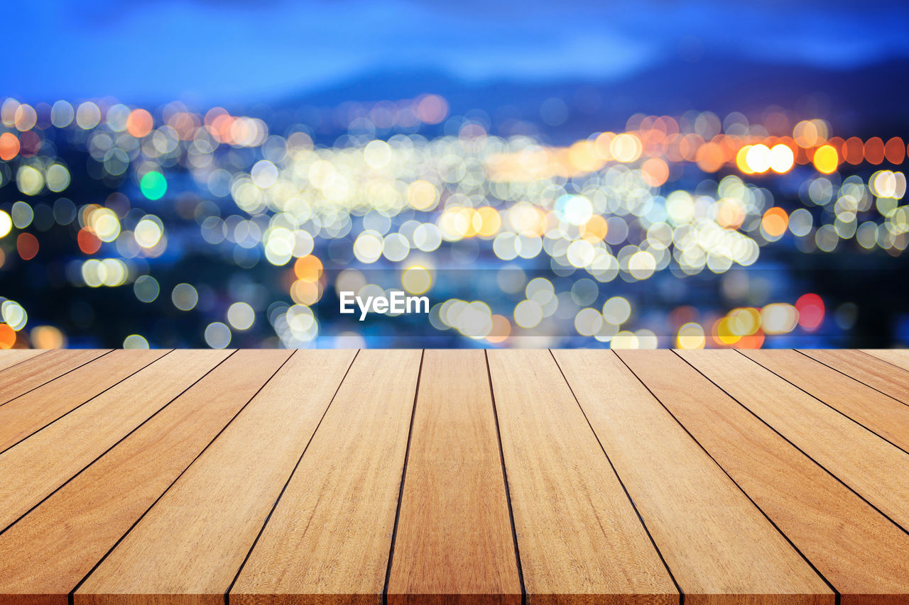 Close-up of wooden table with illuminated city in background