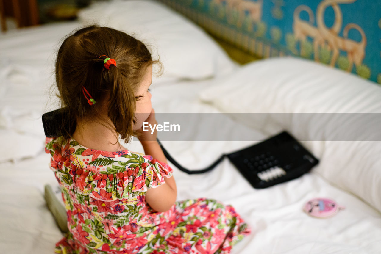 High angle view of girl talking on phone while sitting in bed at home