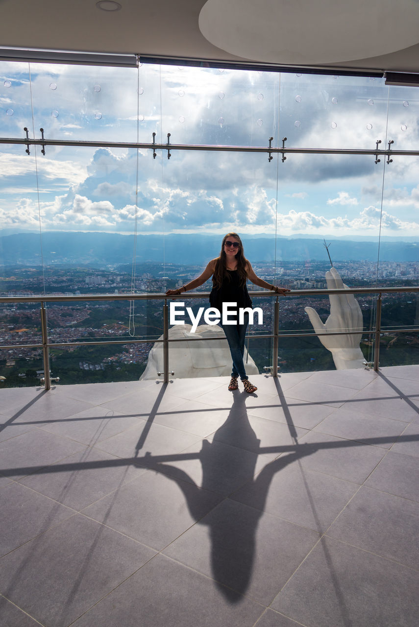 FULL LENGTH OF YOUNG WOMAN STANDING AGAINST SKY