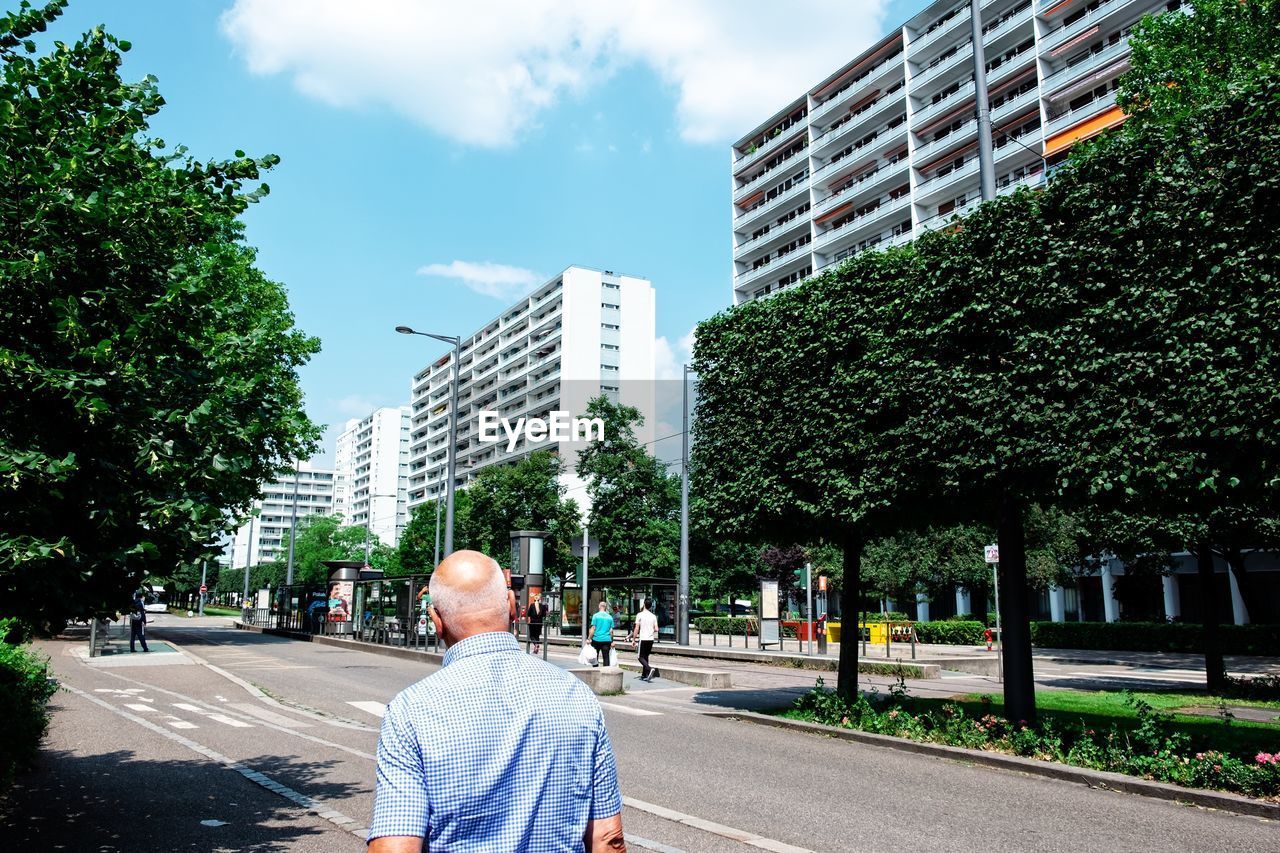 Rear view of man walking on street amidst buildings in city