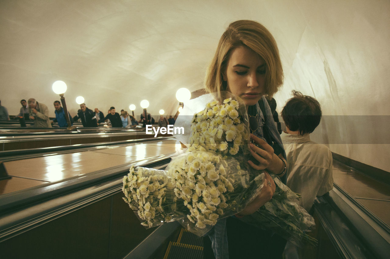 Beautiful woman with flower bouquets standing on escalator