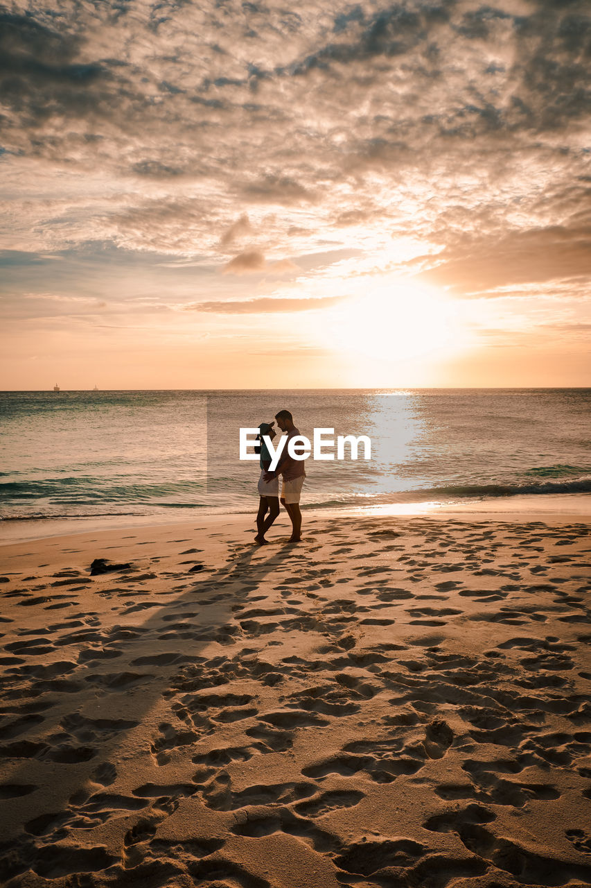 Couple standing on beach against sky during sunset