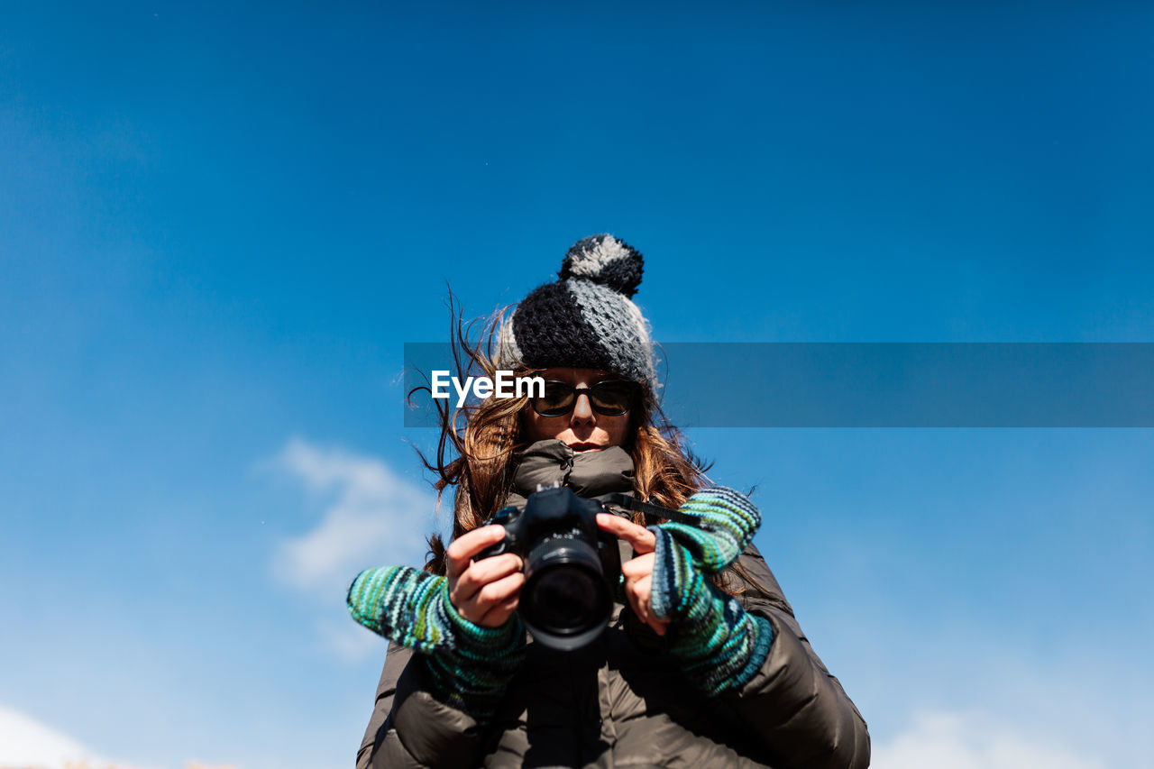Low angle view of man photographing against blue sky