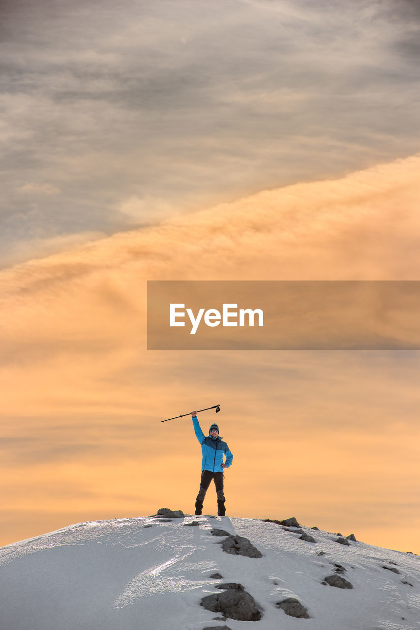 Man climbing on snowcapped mountain against cloudy sky during sunset