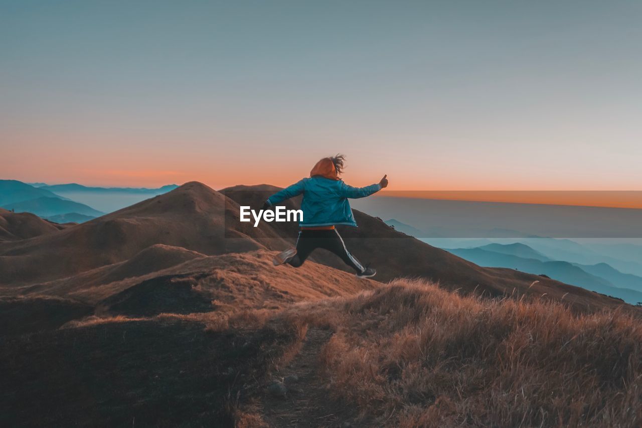 Rear view of man jumping on mountain against clear sky during sunset