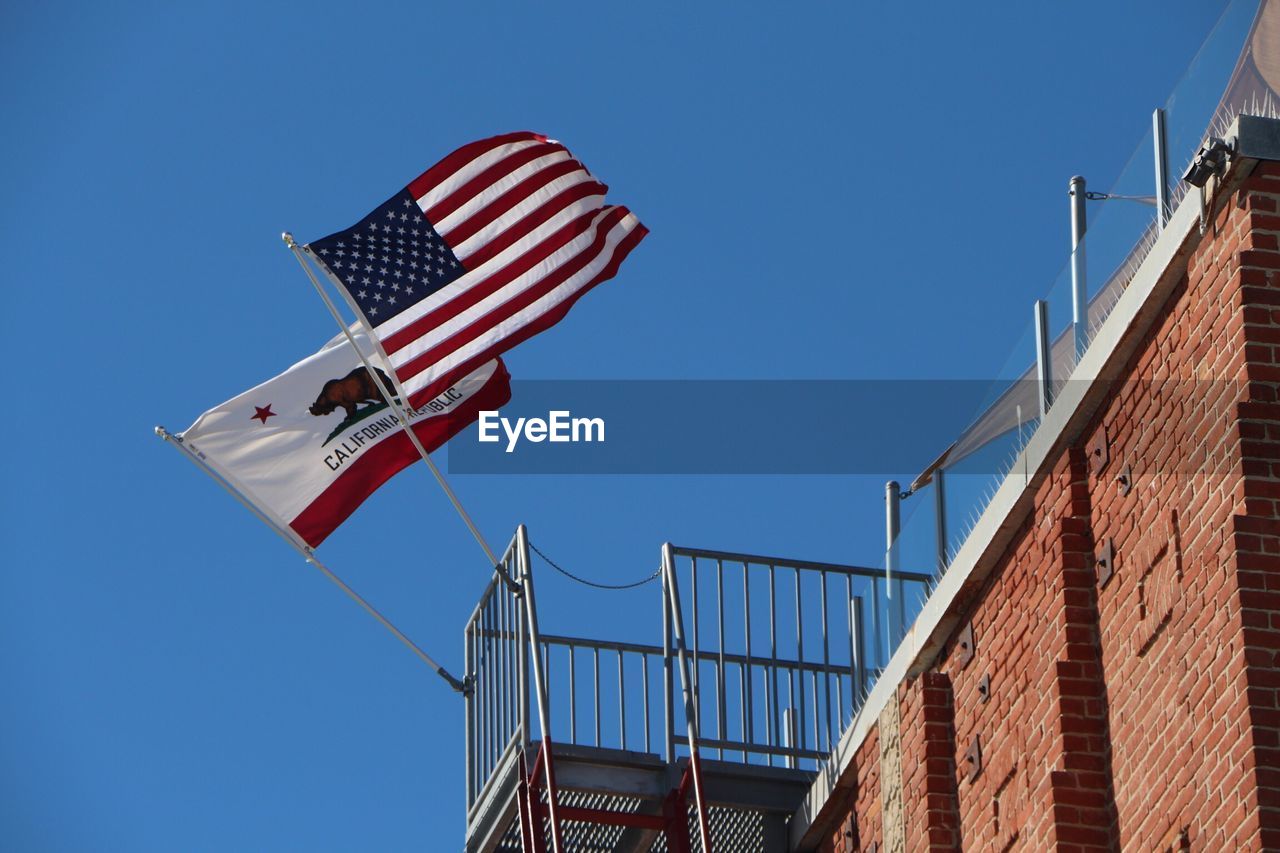 Low angle view of flags on railing against clear blue sky