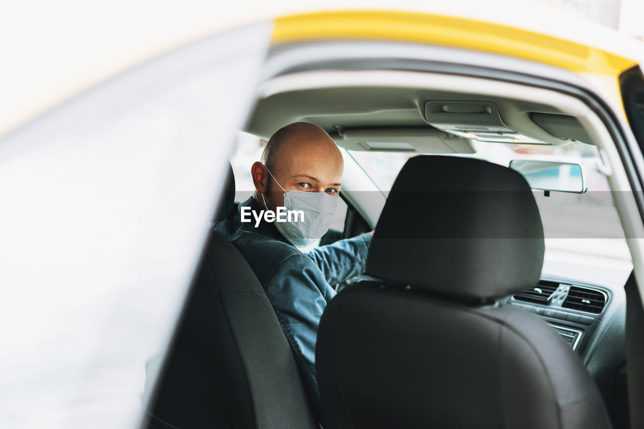 Portrait of man wearing mask sitting in car seen through window